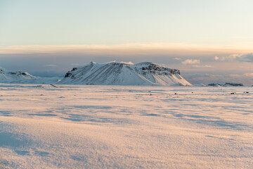 montañas de tierra volcánica nevadas, rodeadas de campos de nieve con el cielo azul claro e iluminadas por las primeras luces del día