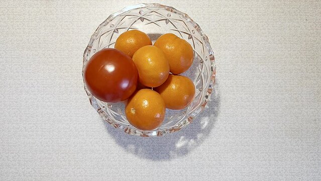 Single tomato is thrown into a vase of tangerines