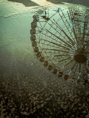 Puddle with reflected Ferris wheel, Italy, Lazio. Reflection in the water of the wheel at sunset