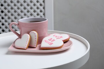 Delicious heart shaped cookies and cup of tea on white table