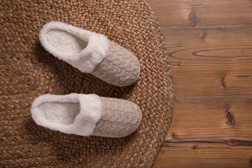 Fototapeta na wymiar Pair of warm stylish slippers and wicker mat on wooden floor, flat lay. Space for text