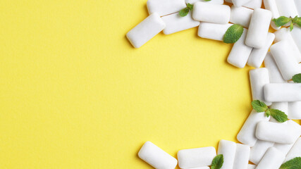 Tasty chewing gums and mint leaves on yellow background, flat lay. Space for text