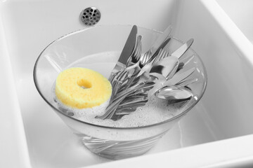 Washing silver spoons, forks and knives in kitchen sink