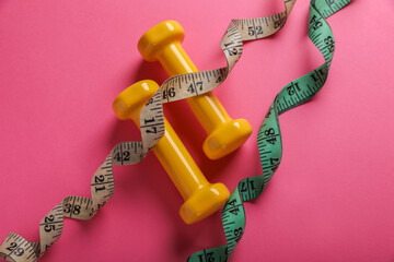Measuring tapes and dumbbells on pink background, flat lay. Weight control concept