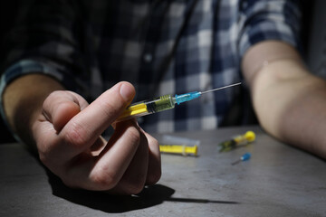 Drug addiction. Man with syringe at grey table, closeup