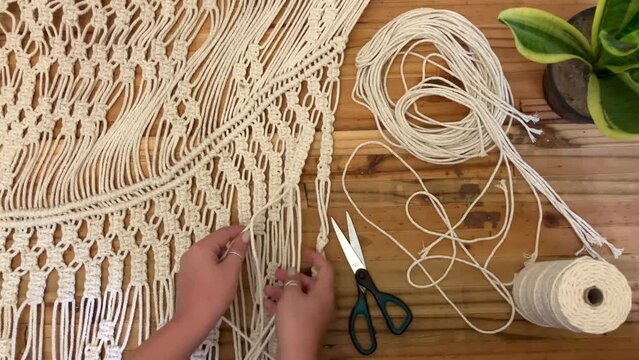 A young woman hand crafting a Macrame wall hanging on a wooden background 
