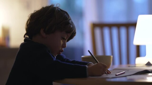 One concentrated child drawing on paper. Candid creative kid doing art at night at home