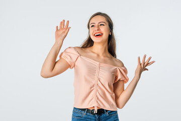 Fototapeta na wymiar Portrait of enthusiastic brunette young woman raise hands up, as dancing and looks aside with a happy smile on face, stands against white background. Happy people