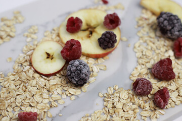 healthy tasty hearty high-calorie oatmeal with fruits and raspberries and blackberries and apples on a white kitchen board. for screensavers signboards labels banners flyers menus
