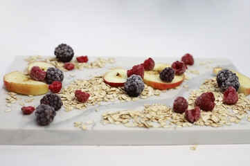 healthy tasty hearty high-calorie oatmeal with fruits and raspberries and blackberries and apples on a white kitchen board. for screensavers signboards labels banners flyers menus