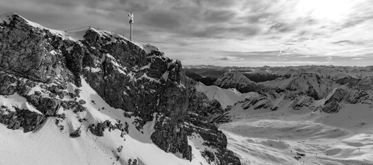 “Zugspitze“ panorama with summit cross is the hightest mountain peak in the bavarian alps in Germany. Wide angle winter panorama near Garmisch-Partenkirchen and Austria, black and white greyscale.