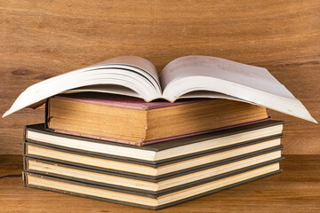 Closeup view stack of dark hardcover books with an open white pages book on wooden table.