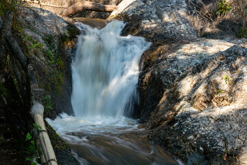 Natural clear mountain stream water flowing down over boulders in the shade of trees at Chae Son National Park in Thailand.