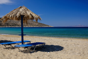 Obraz na płótnie Canvas Sun beds and a sun umbrella at the amazing beach of Agia Theodoti in Ios Greece