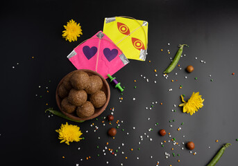 Til Gul OR Sweet Sesame Laddu with Kite model, haldi Kumkum and sugar crystals for Makar Sankranti festival over black background.