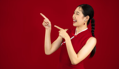 Asian woman in red chinese dress smiling face fingers pointing copy space red background. Chinese New Year concept.