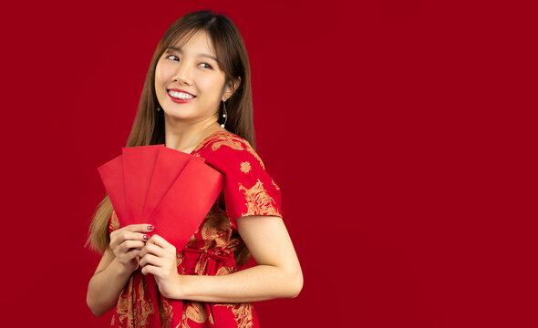 Young beautiful asian woman in red dress holding and showing red envelopes of Chinese New Year bunus and gift on red background.