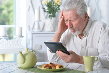 senior man using tablet while drinking tea at kitchen