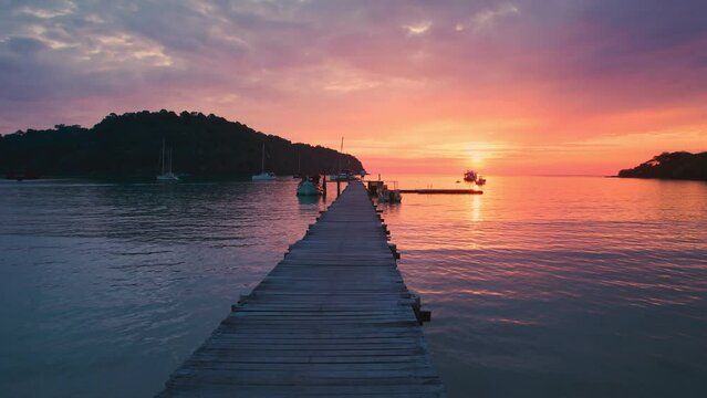 Aerial view of colorful sunset over the tropical sea with wooden pier and sightseeing boat in summer