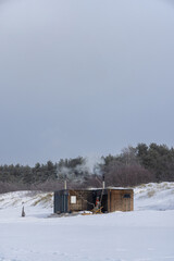 Wooden outdoor sauna with a smoke coming out of chimney on a beautiful cold snowy winter day at the Baltic sea. Well being and healthy life style.