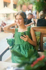 Happy teenage girl sitting in cafeteria with headphones listen to the music