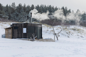 Wooden outdoor sauna with a smoke coming out of chimney on a beautiful cold snowy winter day at the...
