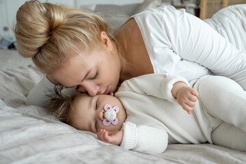 Mom makes baby toddler sleep, lull, kid sucks pacifier. Parent and child lie in bed, mother gently...