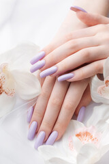 Fototapeta na wymiar Girl's hands with delicate purple manicure and orchid flowers