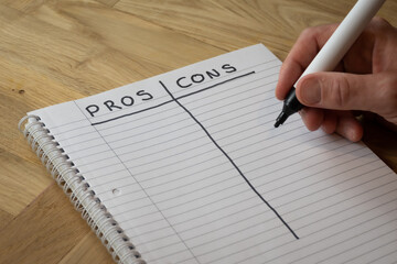 A man writes a list of pros and cons by hand in a notepad on a desk in order to attempt to foresee potential outcomes of various actions to help an important decision making process - 558623349