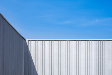 Fototapeta premium Corrugated Steel Industrial Warehouse Building Wall against blue sky background with light and shadow on surface