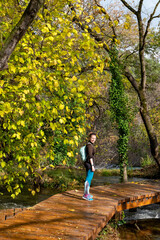 Obraz premium Woman walking in Krka National Park during colorful autumn travel destination in Dalmatia, Croatia, Europe. Female and fall colors leafs on trees. Krka Waterfalls and water in sunny morning light fog.