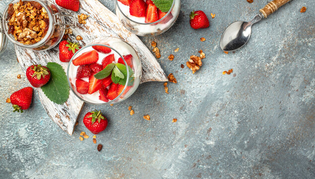 strawberry parfaits with fresh fruit, yogurt and granola on white table, glass jar. Healthy breakfast. Long banner format. top view