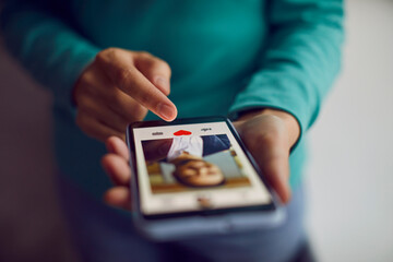 Dating online. Mobile phone in hands of woman who scrolling through profiles of men and pressing red heart button with her finger. Close up of smartphone screen on which modern dating app is open.