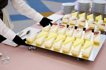 A waiter in black gloves puts a mirrored tray of cheesecakes on the table