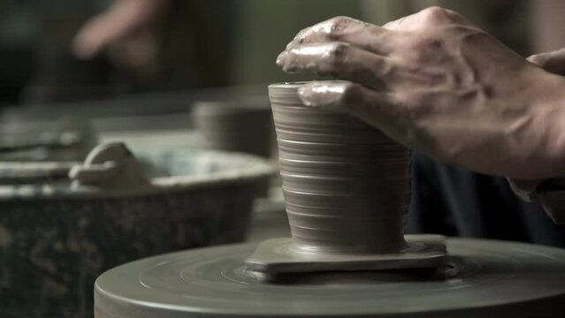 Gental hand and fingers building clay spindle shaping pottery design on wheel by professional potter artist.