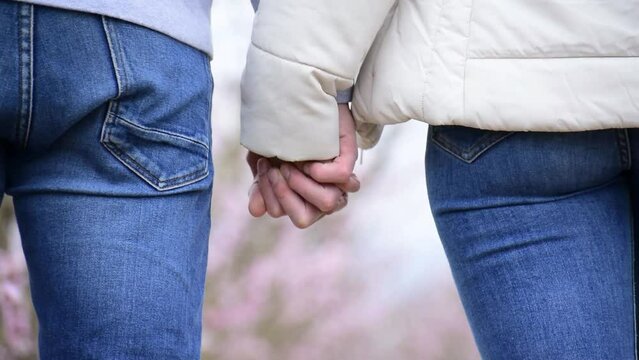 Tight shot of a man and woman holding hands and walking.