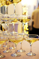 A pyramid of champagne glasses at a party against a background of golden bokeh. Champagne pyramid