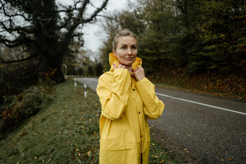 Pretty woman in yellow raincoat walking in rainy weather in the countryside © Ilona