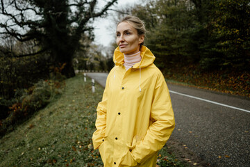 Middle aged woman in yellow raincoat walking in rainy weather in the countryside © Ilona