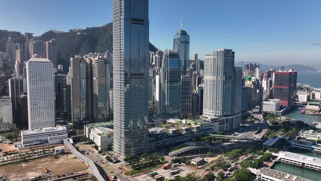 Central financial district with IFC skyscraper and IFC mall in of Hong Kong, iconic mountain 'The Peak' in the background. Aerial pull-away shot during clear day with blue sky