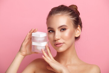 Pretty woman with bare shoulders holds cream on pink