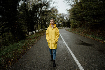 A serene middle-aged woman in a yellow raincoat walks in rainy weather in the countryside. © Ilona