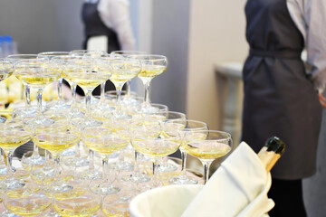 A pyramid of champagne glasses at a party against the backdrop of waiters. champagne pyramid