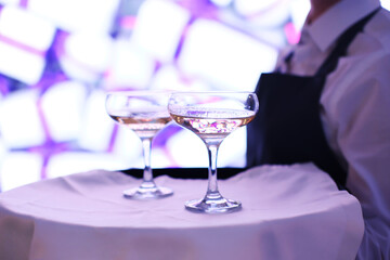 The waiter is holding a tray with two glasses of champagne. Catering for the event