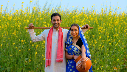 Handsome farmer and his wife in traditional dresses standing in their mustard  or sarso field - Indian Model . Medium shot of an Indian traditional married couple smiling cheerfully at each other -...