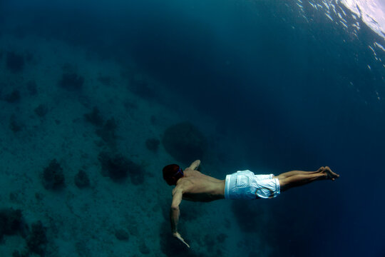 Underwater view of a man swimming deep into the tropical waters off Mana Island, Fiji.