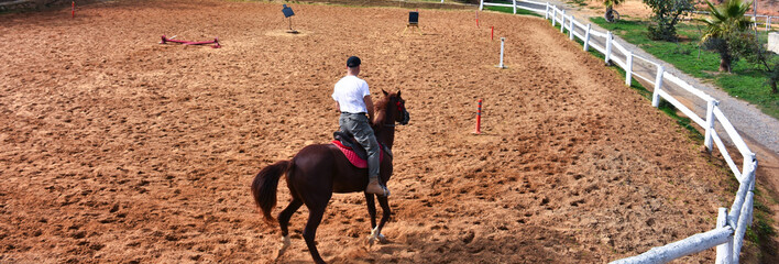 A man riding a horse with his back turned, is training with a horse at the horse farm.