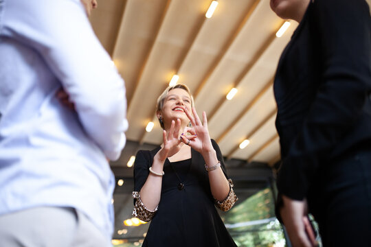 Three young business colleagues having fun conversation and making offensive hand gestures. Successfull startup team brainstorming after work hours in a modern cafe.