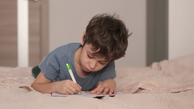 Little asian boy draws or writes in the bed. Little kid draw or hand writing in diary by pencil. cozy home atmosphere