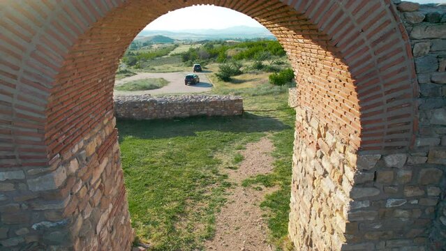 Aerial view of man doing yoga exercise sitting on archaeological site arch at sunset